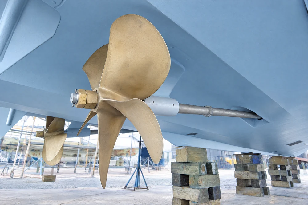 Bronze propeller, shaft, and strut beneath a hauled-out yacht.