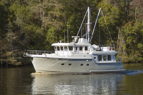 Motor yacht underway beside a wooded shoreline.
